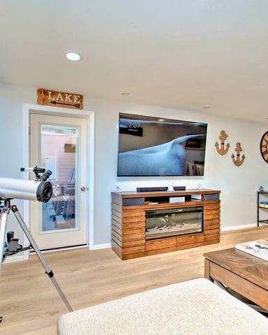 Open-plan living and dining area with exposed beam ceiling, large windows overlooking water, dining table, and seating area