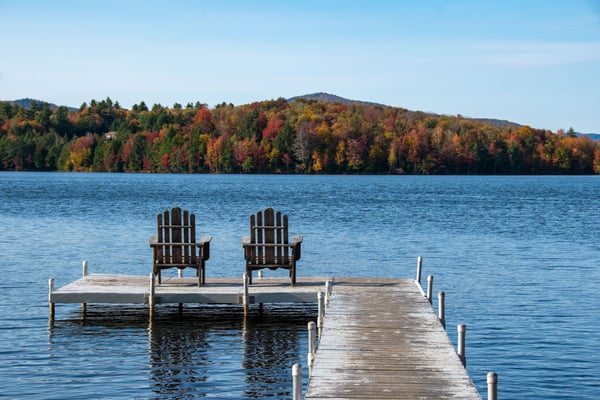 Waterfront property with lawn, dock, and shaded seating area overlooking river surrounded by trees
